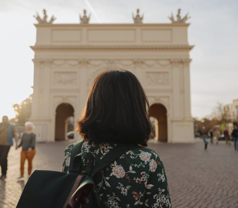 Een vrouw met rugzak kijkt naar de Brandenburger Tor in het zachte avondlicht, waar geschiedenis en rust samen een van de bijzondere Geheimtips Potsdam vormen.