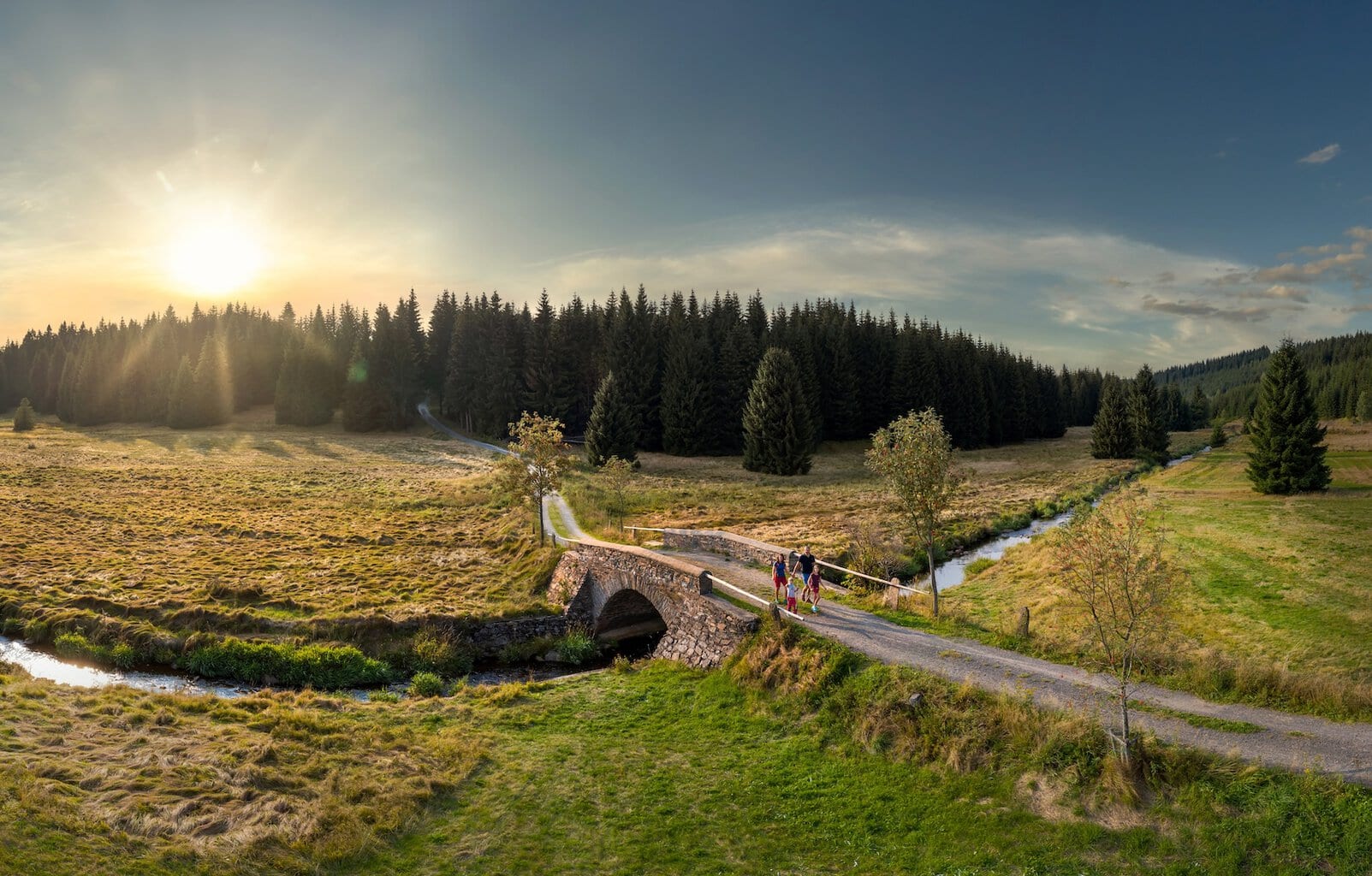 Familie wandelt in het avondlicht over een stenen brug in het Schwarzwassertal in het Erzgebirge