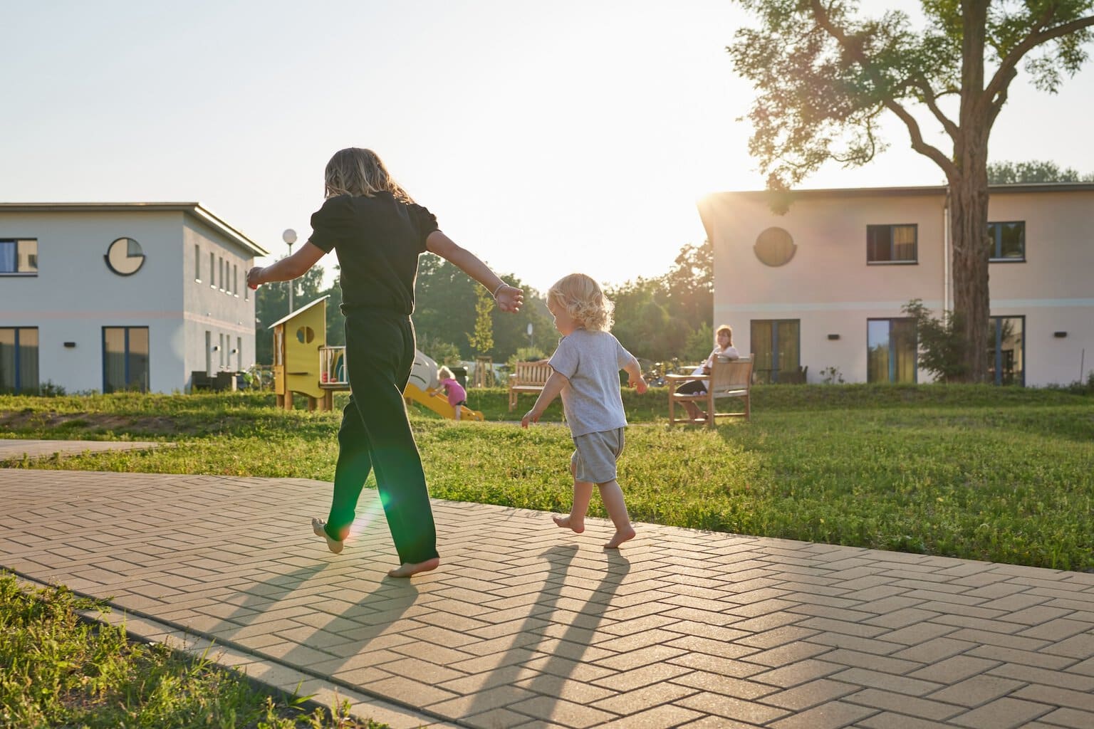 Een kind en zijn moeder lopen op blote voeten over het pad langs een speeltuin en de huizen van het familieresort op Usedom, Mecklenburg-Vorpommern