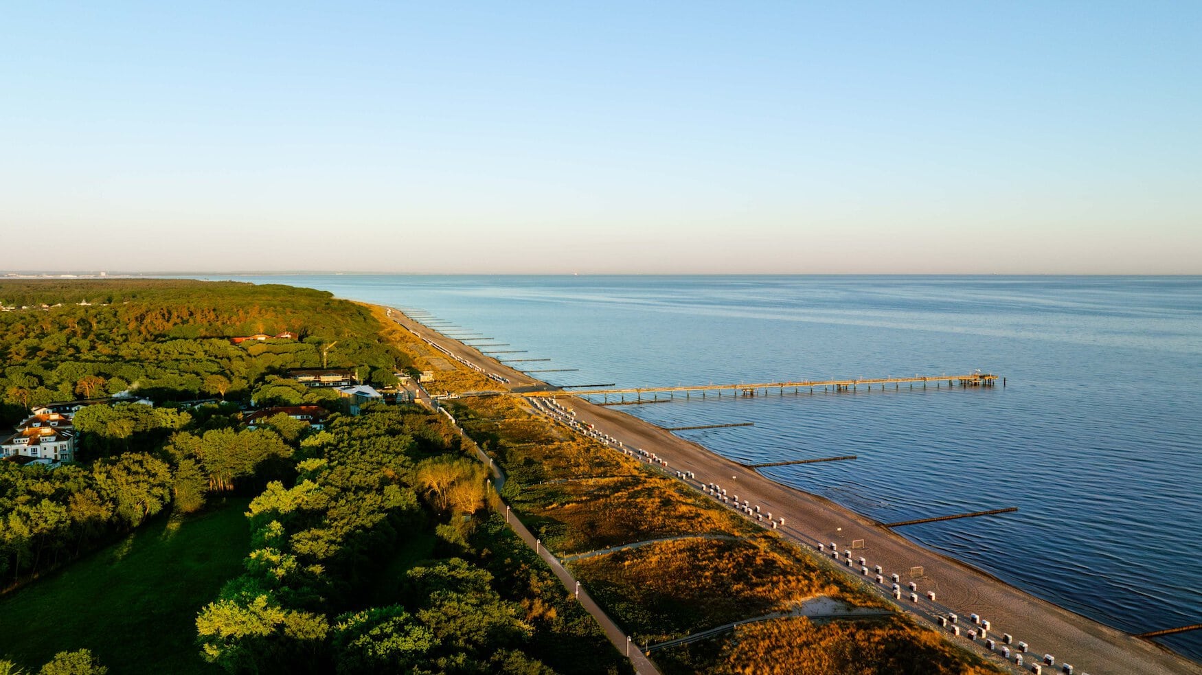 Luchtfoto van de Oostzeekust bij Graal-Müritz met de Seebrücke, rijen strandkorven en het kustbos dat tot vlak aan het strand reikt.