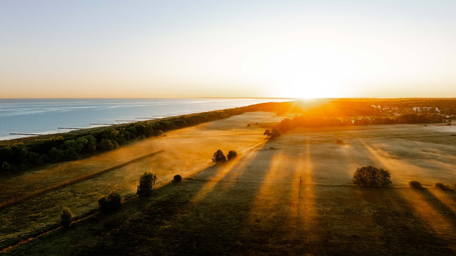 Zonsopkomst boven de velden en het kustbos aan de Oostzee bij Graal-Müritz, met lange lichtstralen over het landschap.