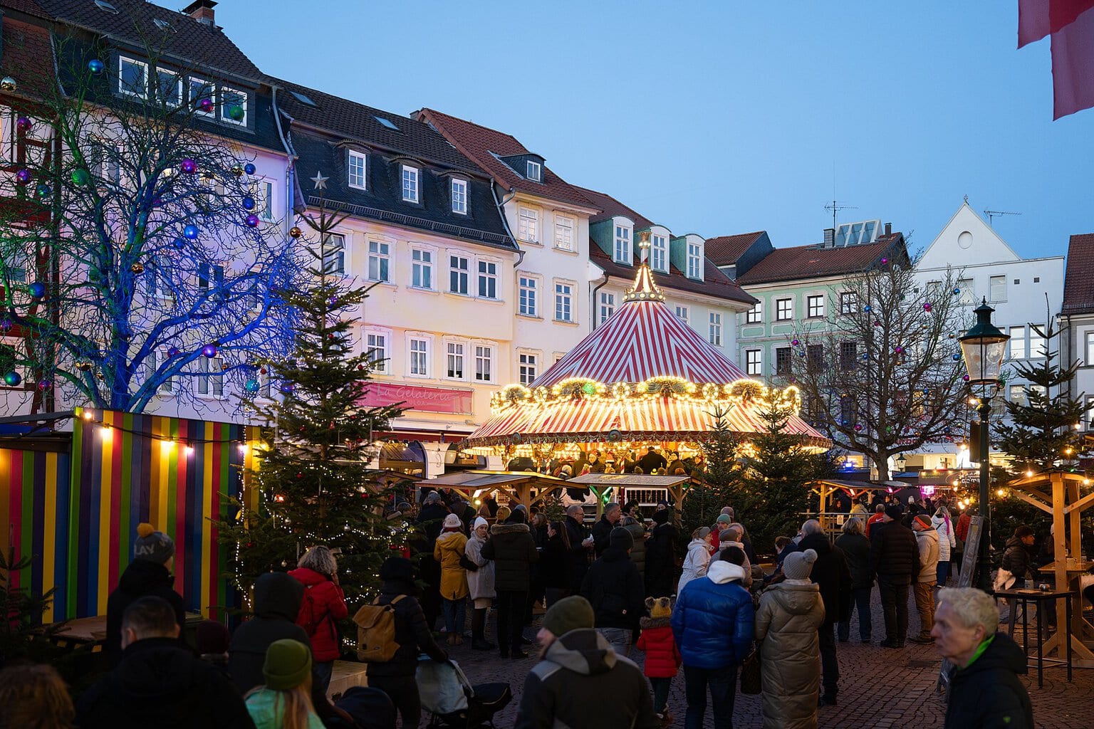 Verlichte nostalgische carrousel met rood-wit dak tussen oude stadshuizen in Fulda