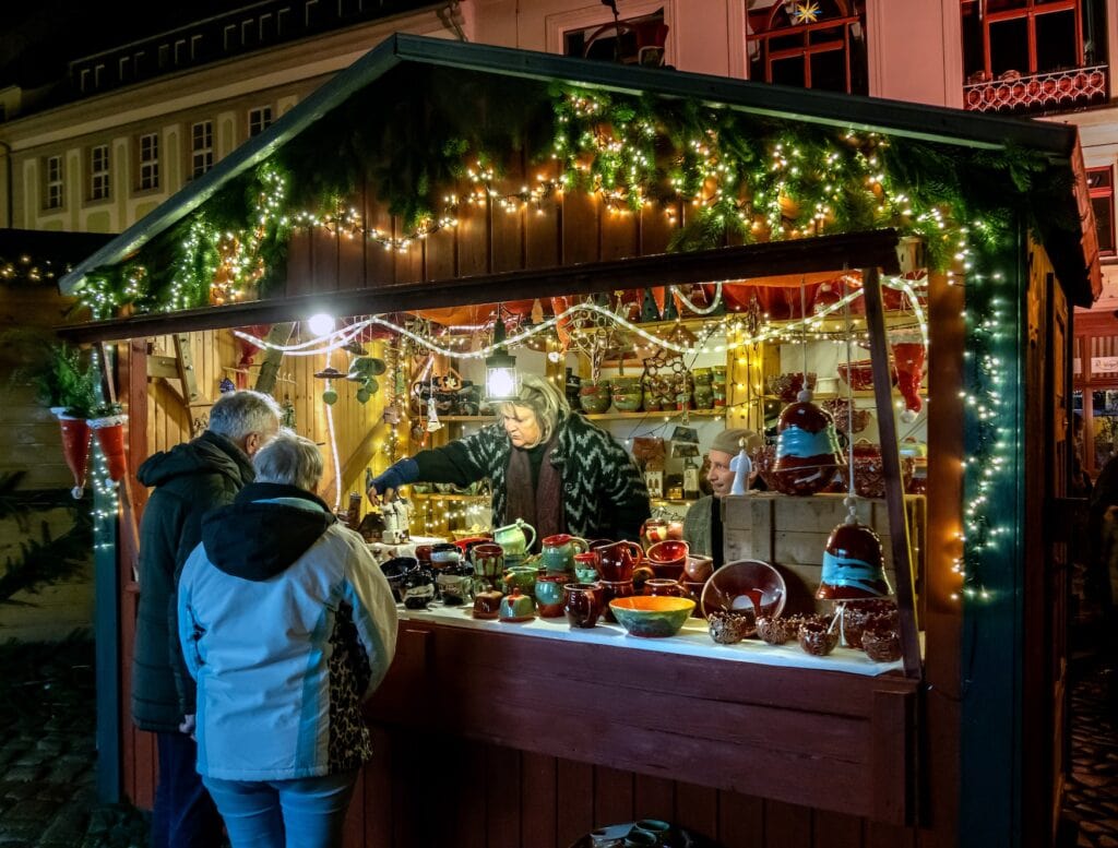 Bezoekers bij een verlichte kraam met aardewerk op de Wenzelsmarkt in Bautzen