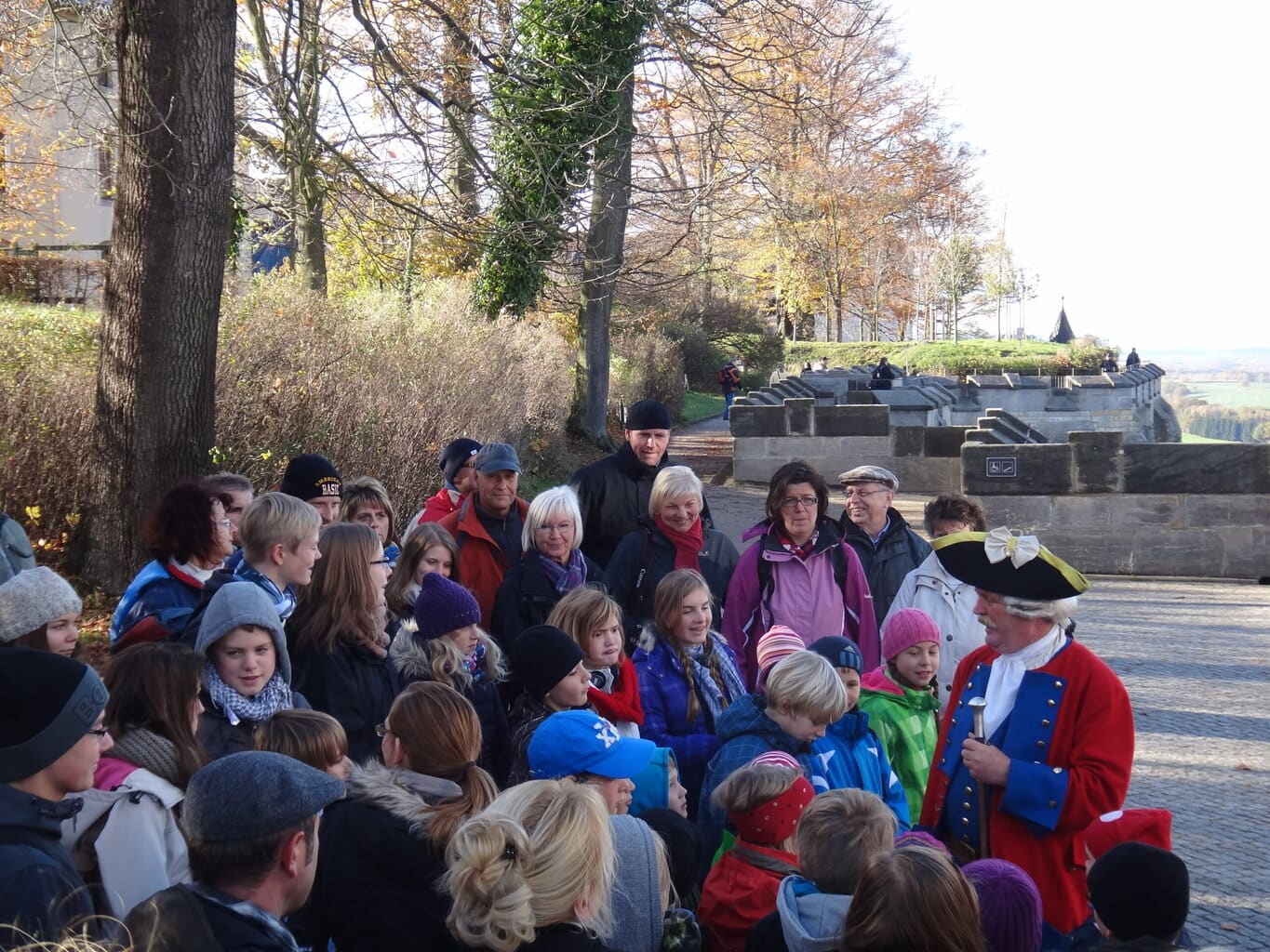 Kinderen luisteren aandachtig naar een gids in historisch kostuum op de vesting Königstein, waar de Saksisch-Zwitserland geschiedenis tot leven komt.