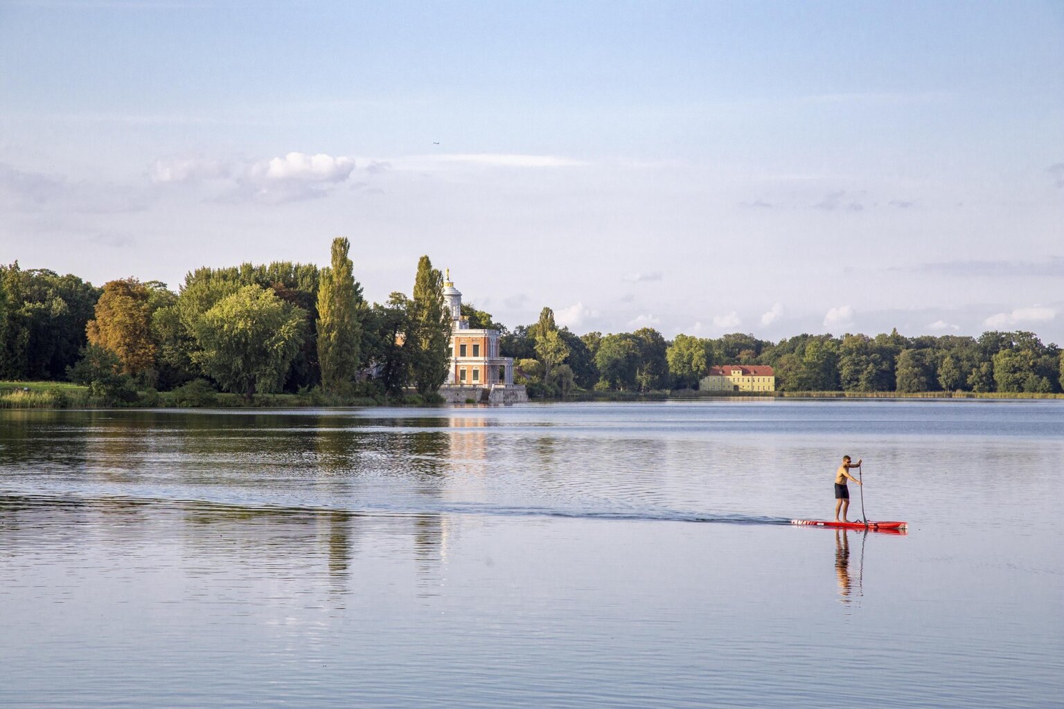 Een man glijdt op zijn board over het stille meer bij Potsdam, omringd door paleizen en bomen – een van de rustgevende Geheimtips Potsdam.