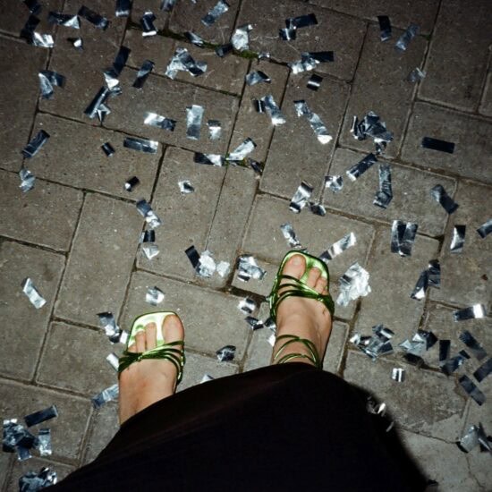 Glinsterend confetti op straat na een Stuttgart party, waar dansende voeten in groene sandalen herinneren aan de nacht vol ritme en vrijheid.