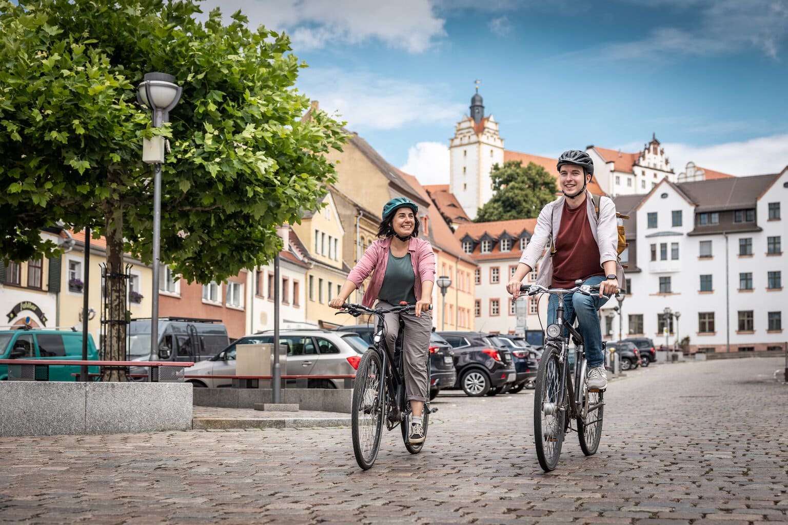 Twee fietsers rijden over het marktplein in de oude binnenstad van Colditz. Op de achtergrond is het kasteel van Colditz te zien.
