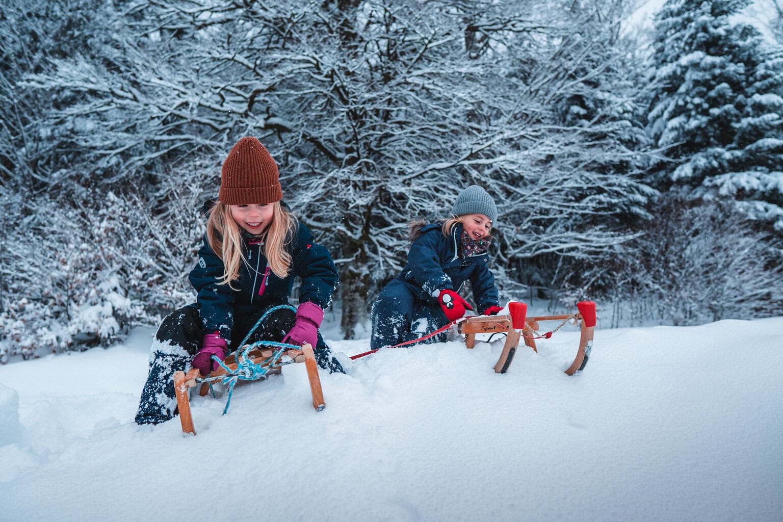 Twee kinderen lachen terwijl ze met hun slee door verse sneeuw glijden, een speels moment vol vreugde en puur Sneeuwplezier Zwarte Woud.
