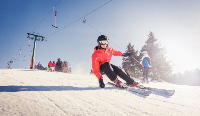 Een skiër snijdt door glinsterende sneeuw onder een stralende hemel, waar snelheid en zonlicht samen het ultieme Sneeuwplezier Zwarte Woud tonen.
