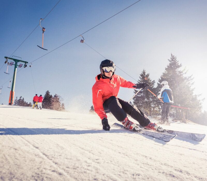 Een skiër snijdt door glinsterende sneeuw onder een stralende hemel, waar snelheid en zonlicht samen het ultieme Sneeuwplezier Zwarte Woud tonen.