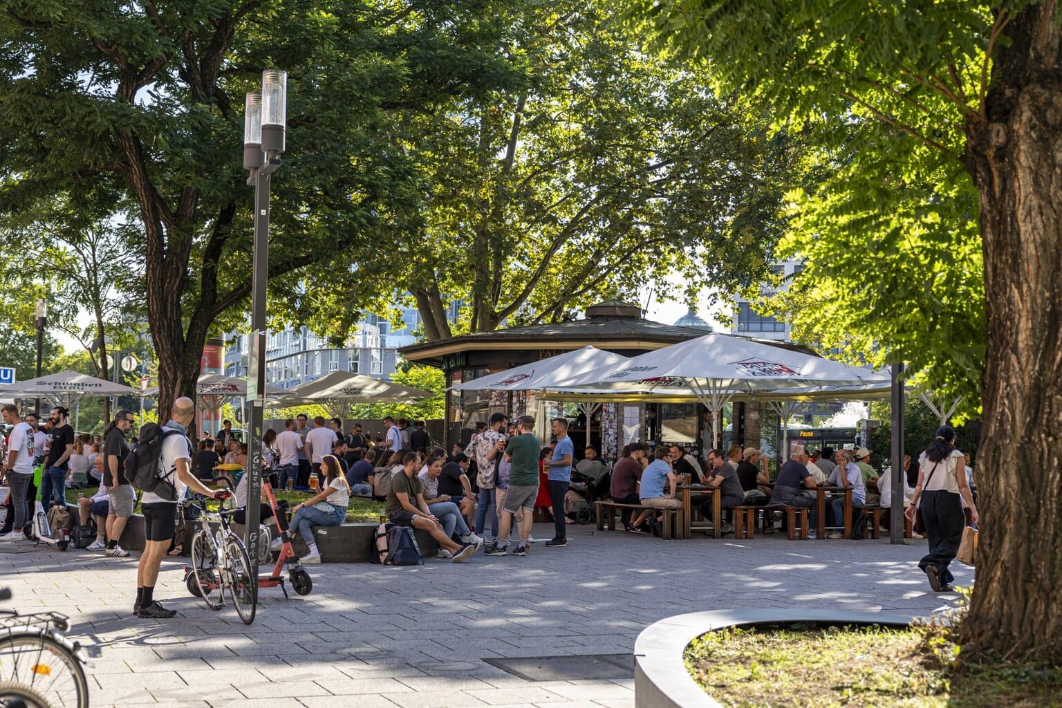 Zonnige middag in een stadspark vol mensen die lachen, drinken en genieten onder groene bomen, een levendige aanloop naar een Stuttgart party.