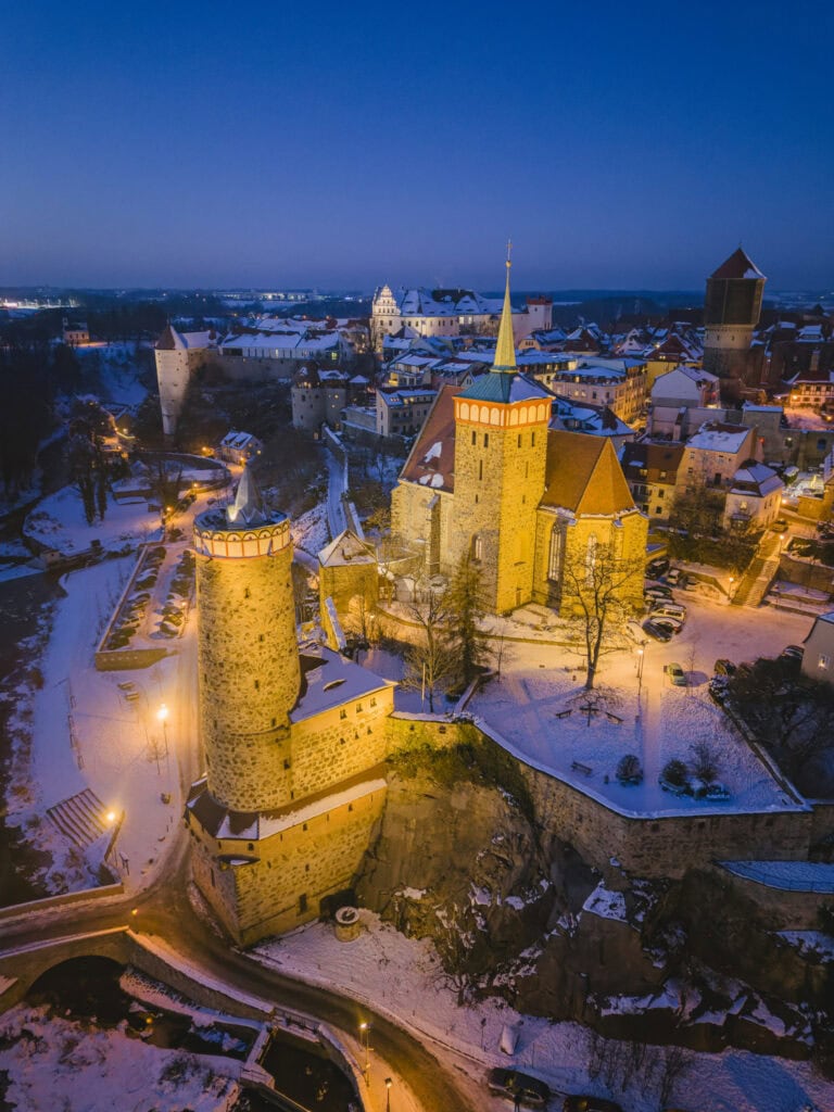 Verlichte Alte Wasserkunst en Michaëlskerk boven de besneeuwde Spree in Bautzen tijdens het blauwe uur