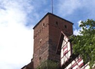 Uitzicht op de historische toren van de Kaiserburg in Neurenberg, met vakwerkhuizen en een wapperende rood-witte vlag onder een blauwe hemel. Een sfeervol hoogtepunt voor activiteiten in Neurenberg tijdens een weekendje weg.
