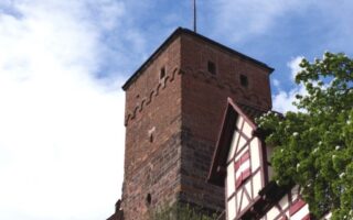 Uitzicht op de historische toren van de Kaiserburg in Neurenberg, met vakwerkhuizen en een wapperende rood-witte vlag onder een blauwe hemel. Een sfeervol hoogtepunt voor activiteiten in Neurenberg tijdens een weekendje weg.