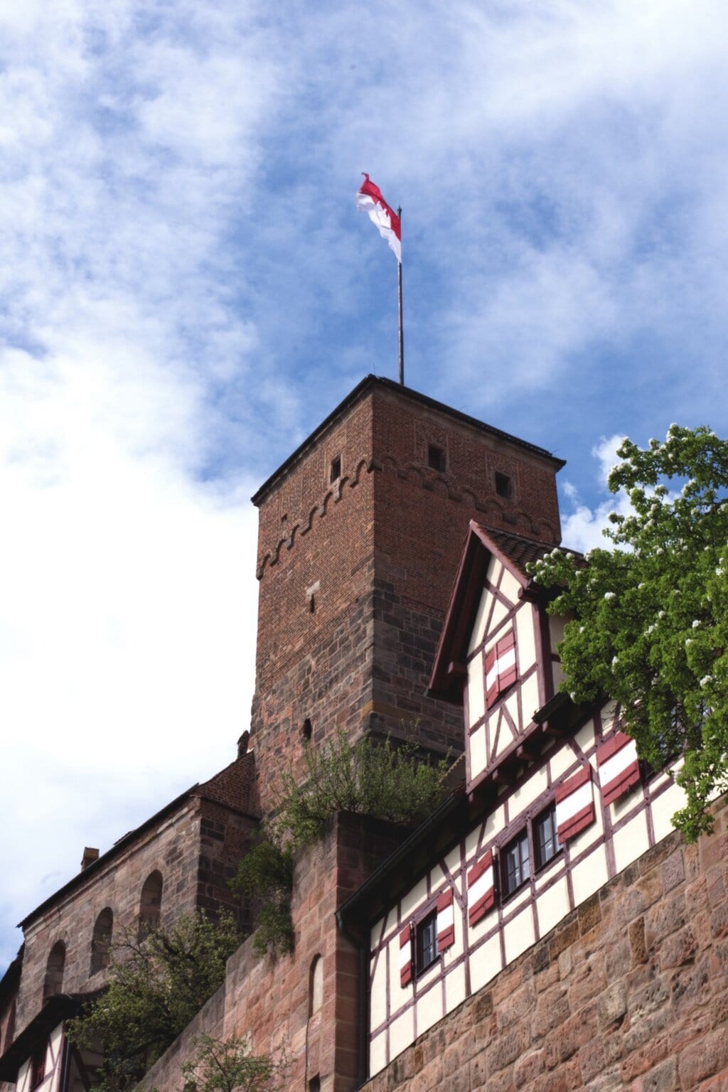 Uitzicht op de historische toren van de Kaiserburg in Neurenberg, met vakwerkhuizen en een wapperende rood-witte vlag onder een blauwe hemel. Een sfeervol hoogtepunt voor activiteiten in Neurenberg tijdens een weekendje weg.