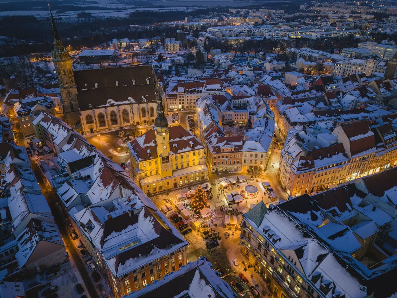 Besneeuwde oude stad van Bautzen tijdens het blauwe uur vanuit de lucht, met het verlichte stadhuis, de Sint-Petrusdom en de Wenzelsmarkt met kerstboom op de Hauptmarkt