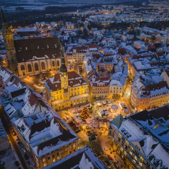 Besneeuwde oude stad van Bautzen tijdens het blauwe uur vanuit de lucht, met het verlichte stadhuis, de Sint-Petrusdom en de Wenzelsmarkt met kerstboom op de Hauptmarkt