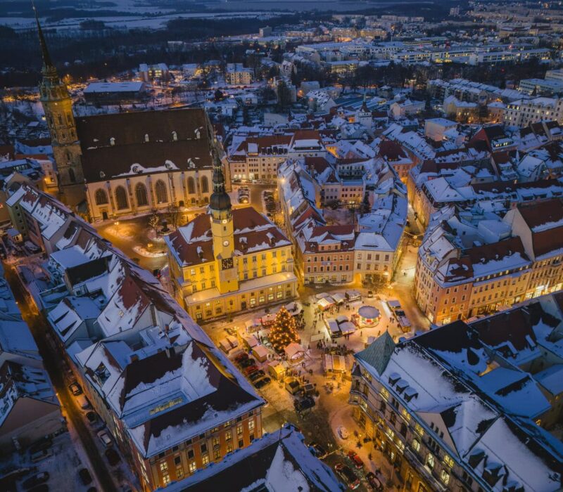 Besneeuwde oude stad van Bautzen tijdens het blauwe uur vanuit de lucht, met het verlichte stadhuis, de Sint-Petrusdom en de Wenzelsmarkt met kerstboom op de Hauptmarkt