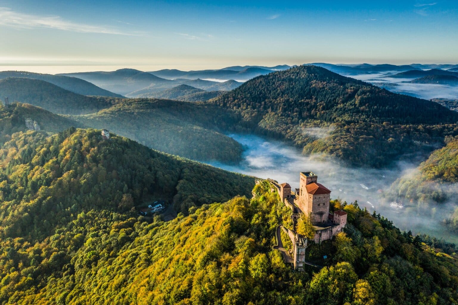 Kasteel Trifels torent boven het mistige Pfälzerwald uit, omringd door groene heuvels en ochtendnevel – een panoramisch decor dat perfect past bij de mooie kastelen in Duitsland.