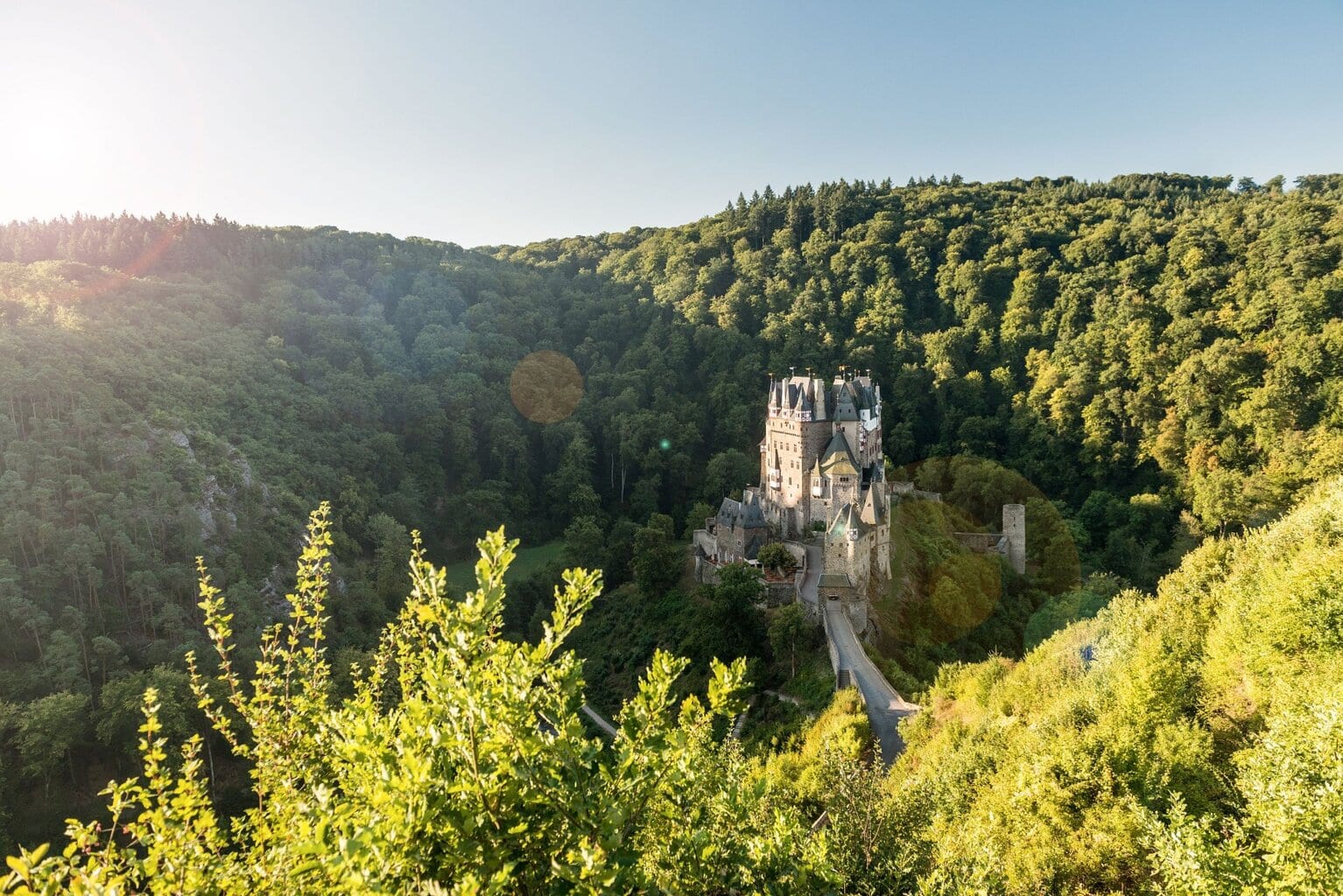 Panoramisch uitzicht op kasteel Eltz, verscholen tussen de groene heuvels en bossen van Rijnland-Palts, een sprookjesachtig decor dat laat zien waarom dit behoort tot de mooie kastelen in Duitsland.