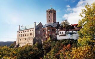 De Wartburg in Thüringen, hoog boven het herfstkleurige landschap, met robuuste torens en vakwerkgebouwen die samen een iconisch beeld vormen van de mooiste kastelen in Duitsland en het leven van ridders en vorsten tot leven brengen.
