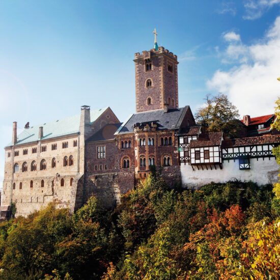 De Wartburg in Thüringen, hoog boven het herfstkleurige landschap, met robuuste torens en vakwerkgebouwen die samen een iconisch beeld vormen van de mooiste kastelen in Duitsland en het leven van ridders en vorsten tot leven brengen.