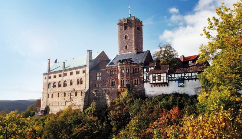 De Wartburg in Thüringen, hoog boven het herfstkleurige landschap, met robuuste torens en vakwerkgebouwen die samen een iconisch beeld vormen van de mooiste kastelen in Duitsland en het leven van ridders en vorsten tot leven brengen.