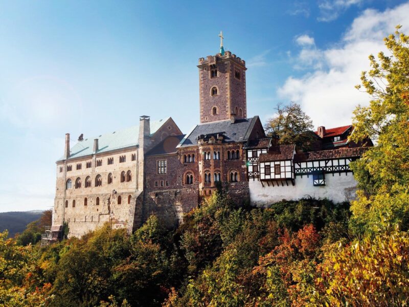 De Wartburg in Thüringen, hoog boven het herfstkleurige landschap, met robuuste torens en vakwerkgebouwen die samen een iconisch beeld vormen van de mooiste kastelen in Duitsland en het leven van ridders en vorsten tot leven brengen.