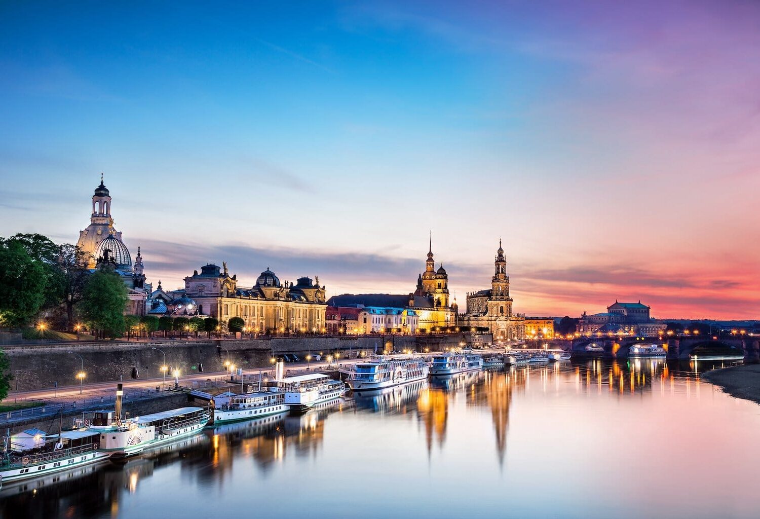 De Elbe ligt op de voorgrond. Daarop varen enkele schepen die aan de oever van de stad Dresden liggen. De lucht is bij de avondzon in rode en paarse tinten die overgaan in het blauw van de hemel. In de Elbe worden het avondlicht en het silhouet van de stad weerspiegeld.