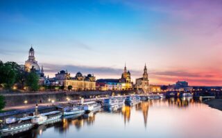 De Elbe ligt op de voorgrond. Daarop varen enkele schepen die aan de oever van de stad Dresden liggen. De lucht is bij de avondzon in rode en paarse tinten die overgaan in het blauw van de hemel. In de Elbe worden het avondlicht en het silhouet van de stad weerspiegeld.