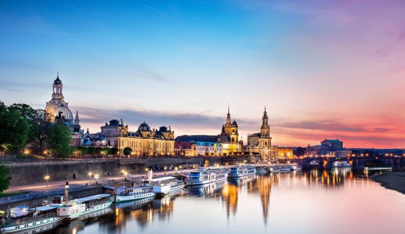 De Elbe ligt op de voorgrond. Daarop varen enkele schepen die aan de oever van de stad Dresden liggen. De lucht is bij de avondzon in rode en paarse tinten die overgaan in het blauw van de hemel. In de Elbe worden het avondlicht en het silhouet van de stad weerspiegeld.