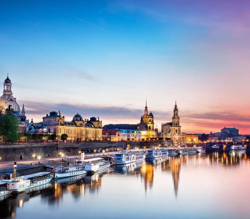 De Elbe ligt op de voorgrond. Daarop varen enkele schepen die aan de oever van de stad Dresden liggen. De lucht is bij de avondzon in rode en paarse tinten die overgaan in het blauw van de hemel. In de Elbe worden het avondlicht en het silhouet van de stad weerspiegeld.