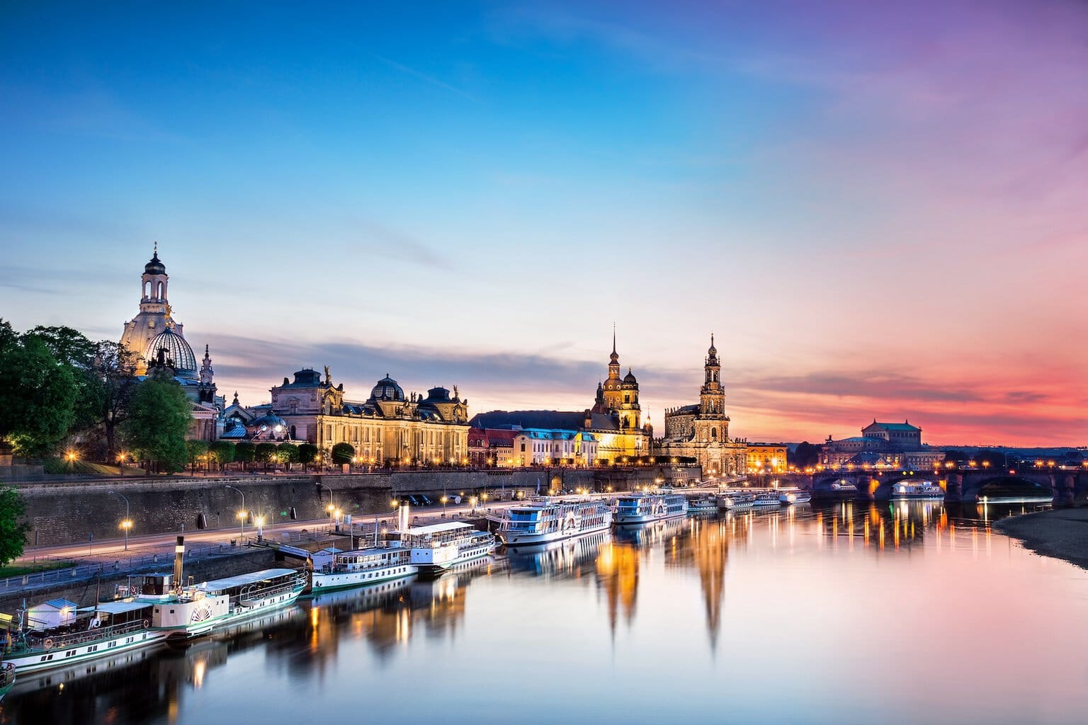 De Elbe ligt op de voorgrond. Daarop varen enkele schepen die aan de oever van de stad Dresden liggen. De lucht is bij de avondzon in rode en paarse tinten die overgaan in het blauw van de hemel. In de Elbe worden het avondlicht en het silhouet van de stad weerspiegeld.
