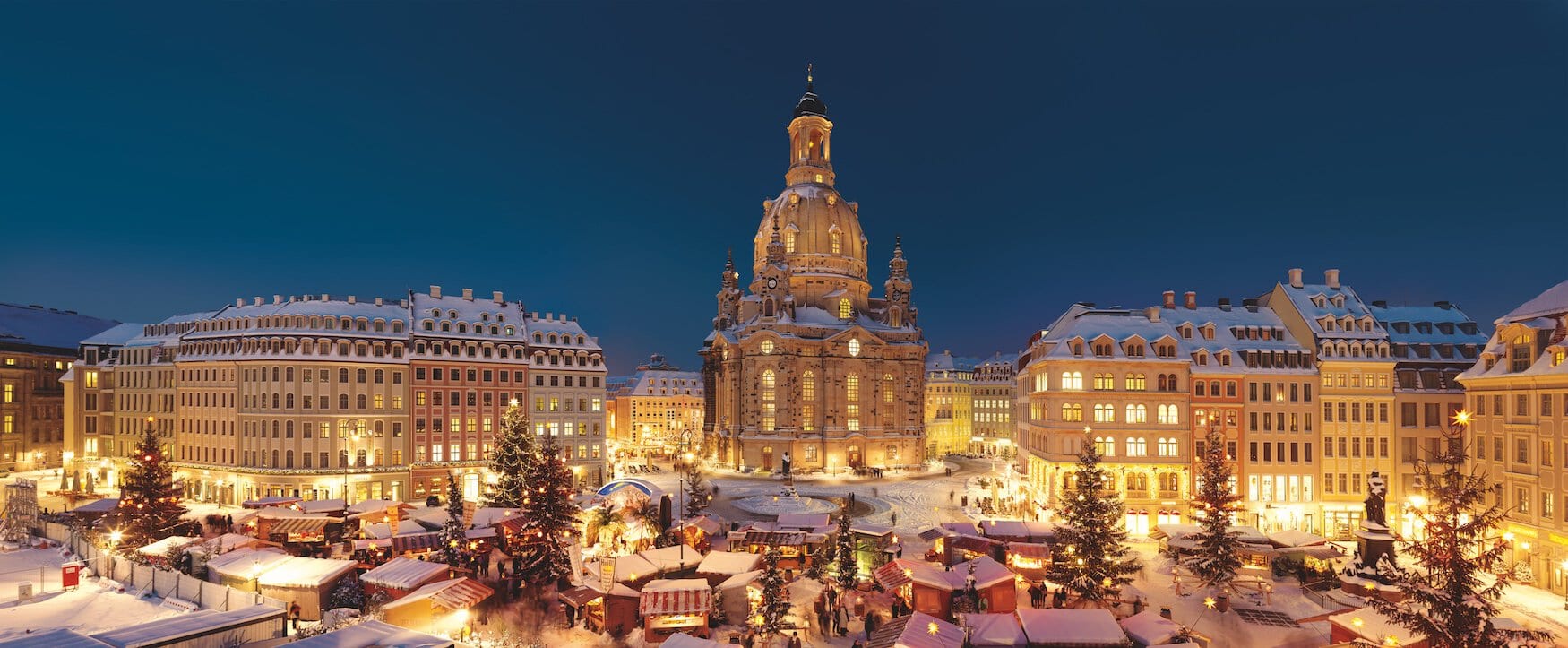 Op de Neumarkt in Dresden vindt een kerstmarkt plaats. Het plein, de marktkraampjes en de Frauenkirche op de achtergrond zijn bedekt met sneeuw. De kerstverlichting verlicht het plein 's avonds.