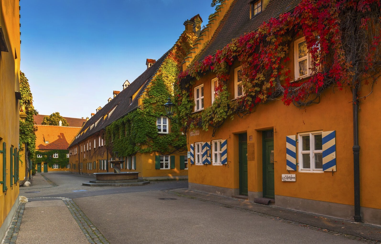 Gele huizen met blauw-witte luiken, begroeid met herfstkleurige rood-groene klimop, vormen de oudste sociale woonwijk ter wereld: de Fuggerei.