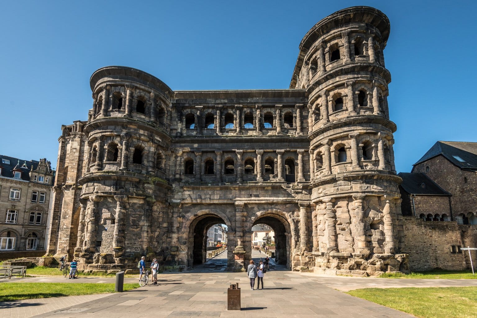Mensen staan bij de Porta Nigra in Trier, Rijnland-Palts, onder een heldere hemel 