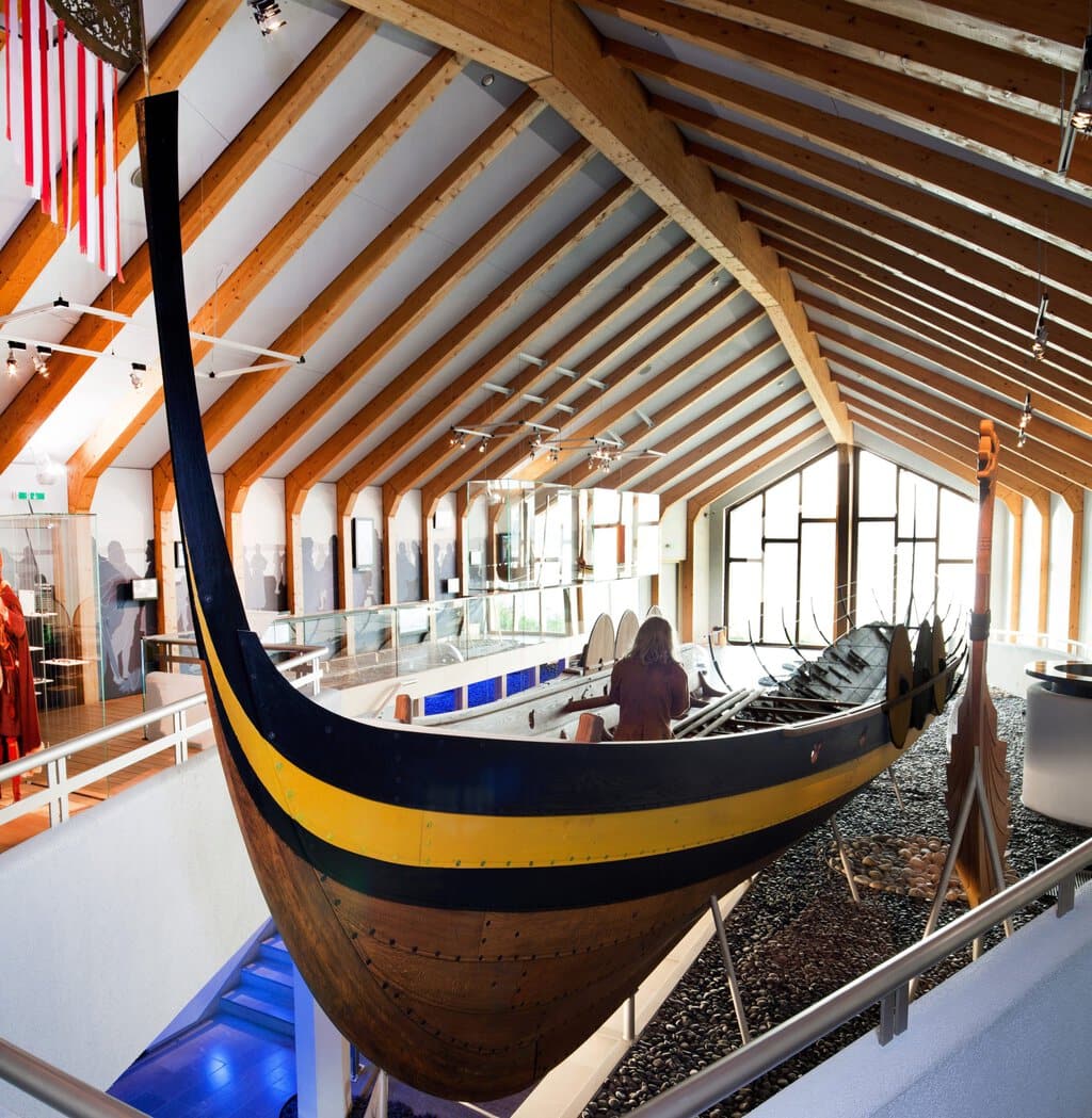 Een bezoeker bekijkt de peddel in het scheepswrak van de Haithabu 1 in het Vikingmuseum Haithabu in Sleeswijk-Holstein. Het wrak bestaat voor de helft uit een gerestaureerde boot; van de andere helft is alleen nog het skelet over. Eromheen is een tentoonstelling van het museum te zien.