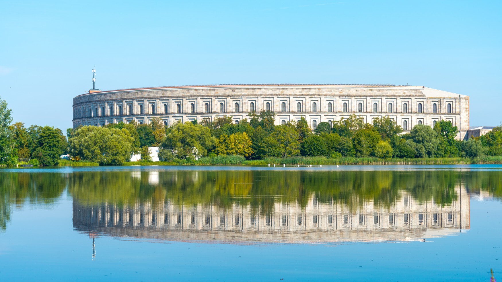 De congreszaal van het documentatiecentrum van het terrein van de Rijkspartijbijeenkomst weerspiegelt zich in de grote Duzendteich in Neurenberg, Beieren, Duitsland