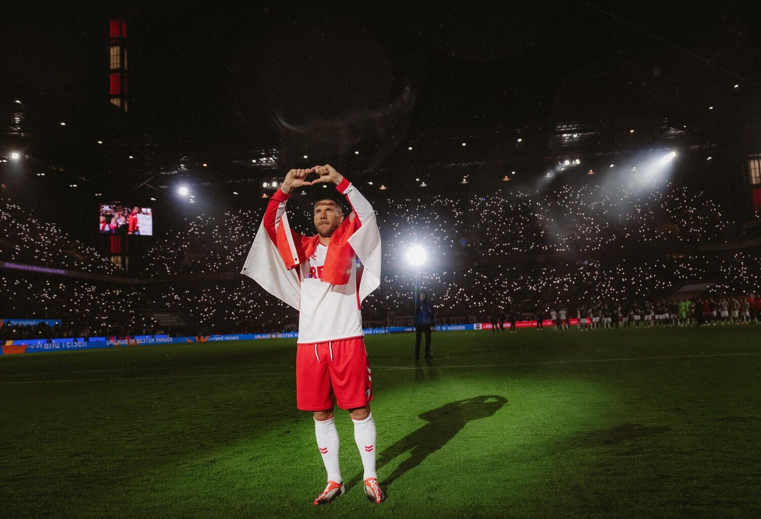 Foto uit de Netflix-documentaire ‘Poldi’: voetballer Lukas Podolski staat in het stadion op het veld in het wit-rode shirt van 1. FC Köln en vormt met zijn vingers een hartje.