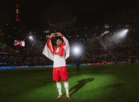 Foto uit de Netflix-documentaire ‘Poldi’: voetballer Lukas Podolski staat in het stadion op het veld in het wit-rode shirt van 1. FC Köln en vormt met zijn vingers een hartje.