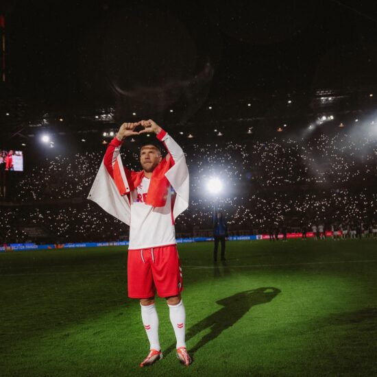 Foto uit de Netflix-documentaire ‘Poldi’: voetballer Lukas Podolski staat in het stadion op het veld in het wit-rode shirt van 1. FC Köln en vormt met zijn vingers een hartje.
