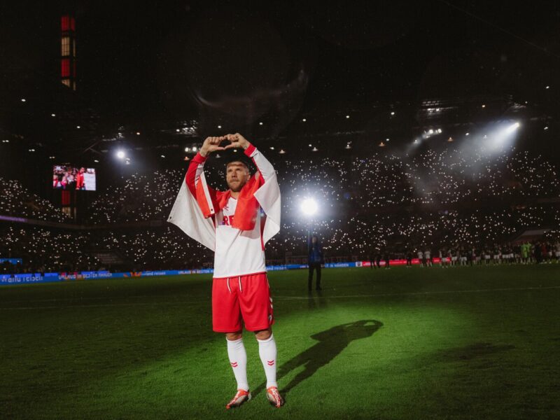 Foto uit de Netflix-documentaire ‘Poldi’: voetballer Lukas Podolski staat in het stadion op het veld in het wit-rode shirt van 1. FC Köln en vormt met zijn vingers een hartje.