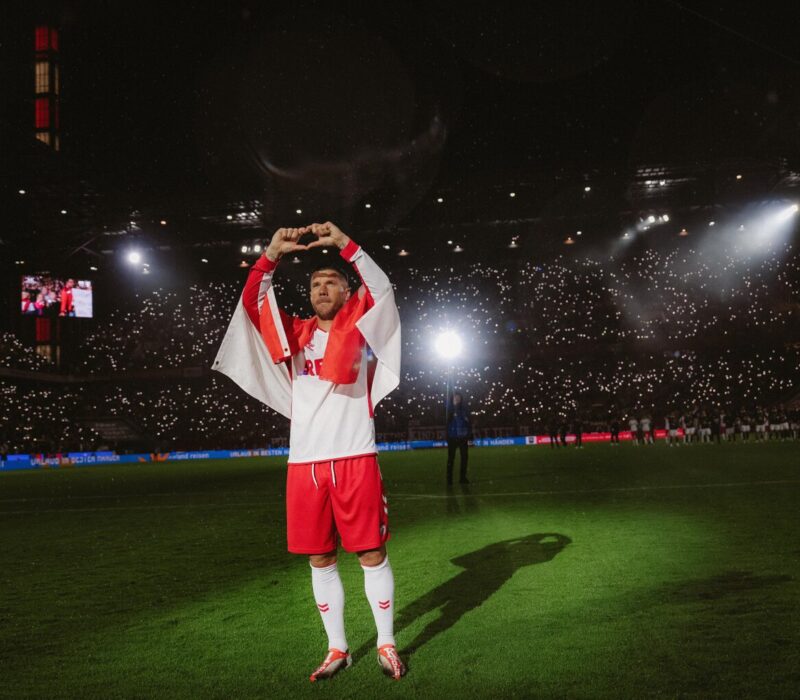 Foto uit de Netflix-documentaire ‘Poldi’: voetballer Lukas Podolski staat in het stadion op het veld in het wit-rode shirt van 1. FC Köln en vormt met zijn vingers een hartje.