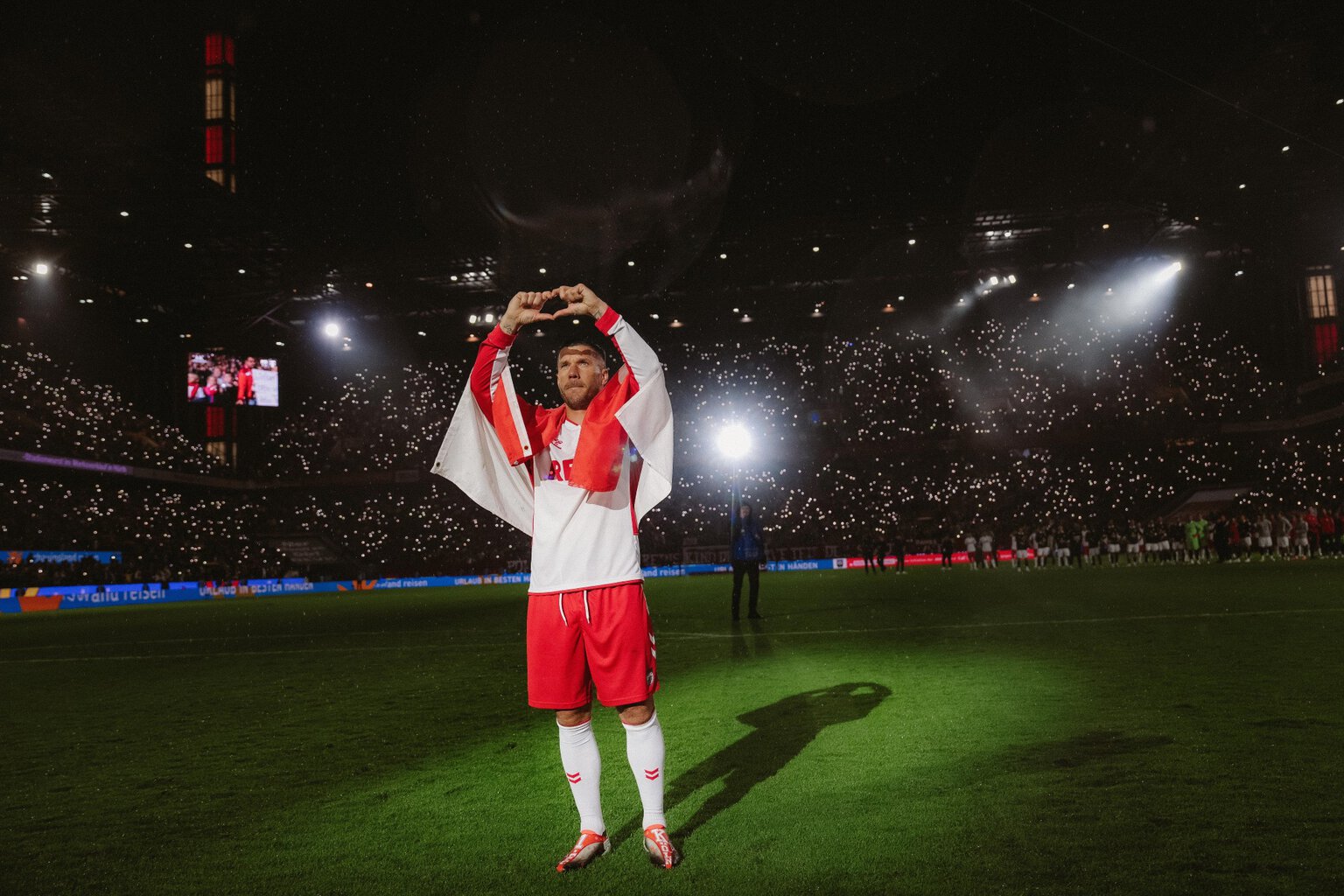 Foto uit de Netflix-documentaire ‘Poldi’: voetballer Lukas Podolski staat in het stadion op het veld in het wit-rode shirt van 1. FC Köln en vormt met zijn vingers een hartje.