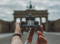 Een hand met een zwarte ring om de duim houdt een souvenir van de Brandenburger Tor voor de echte Brandenburger Tor