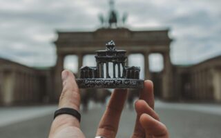 Een hand met een zwarte ring om de duim houdt een souvenir van de Brandenburger Tor voor de echte Brandenburger Tor