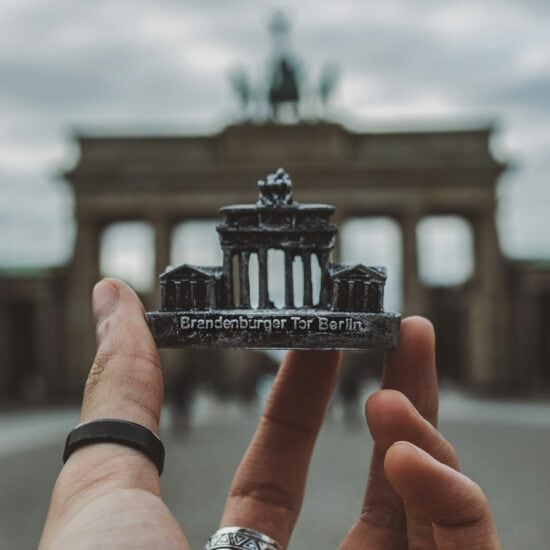 Een hand met een zwarte ring om de duim houdt een souvenir van de Brandenburger Tor voor de echte Brandenburger Tor