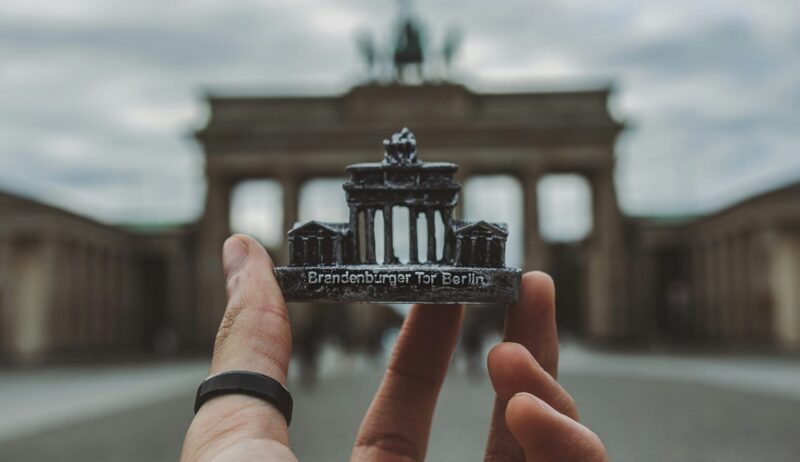 Een hand met een zwarte ring om de duim houdt een souvenir van de Brandenburger Tor voor de echte Brandenburger Tor