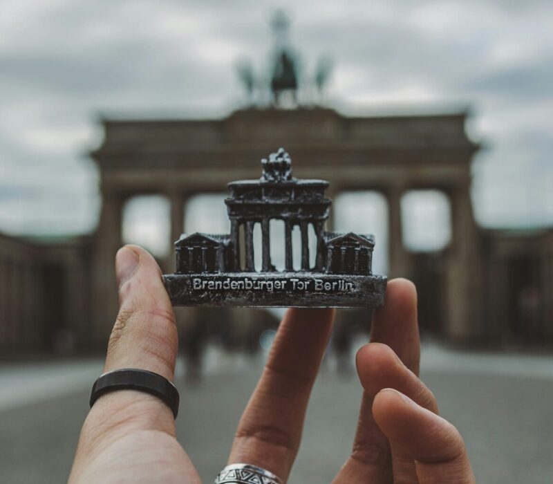 Een hand met een zwarte ring om de duim houdt een souvenir van de Brandenburger Tor voor de echte Brandenburger Tor