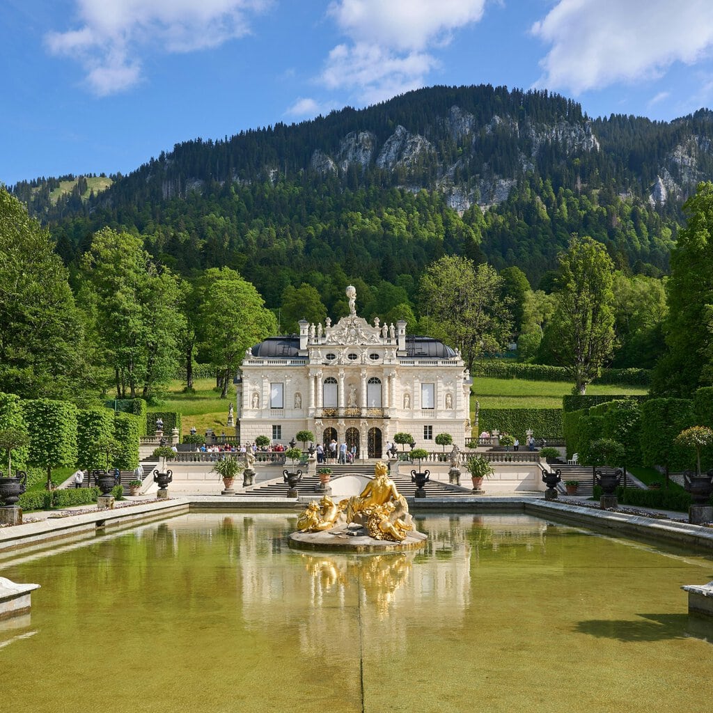 Het UNESCO-werelderfgoed Linderhof ligt tegen de Ammauerse Alpen in Beieren. Daarvoor staat een fontein met een gouden beeld.